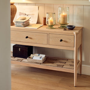 Neptune Frome Console Table in Solid Natural Oak with three deep drawers curved corners a woven undershelf and tapered legs set in a hallway 